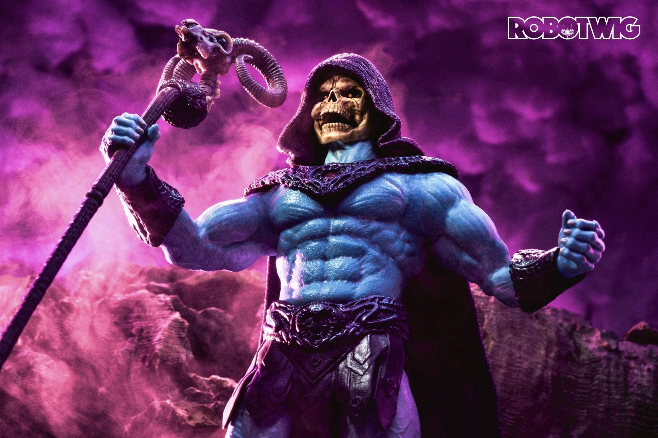 Skeletor stands atop a mountain wailing into the sky arms open and staff in his hand. The sky is a deep pink colour and there's a mythical mist behind him