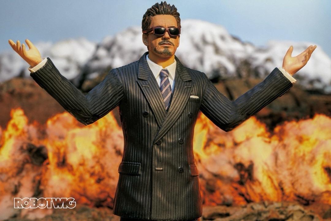 Tony stark shows off his new weapons arms in the air whilst explosions happen behind him