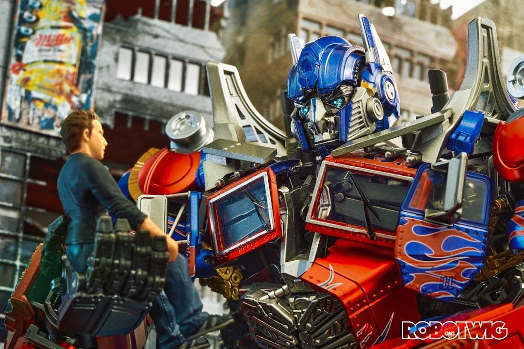 Optimus prime holds Sam Witwicky in his hand whilst they talk to one another. Destroyed buildings can be seen in the background