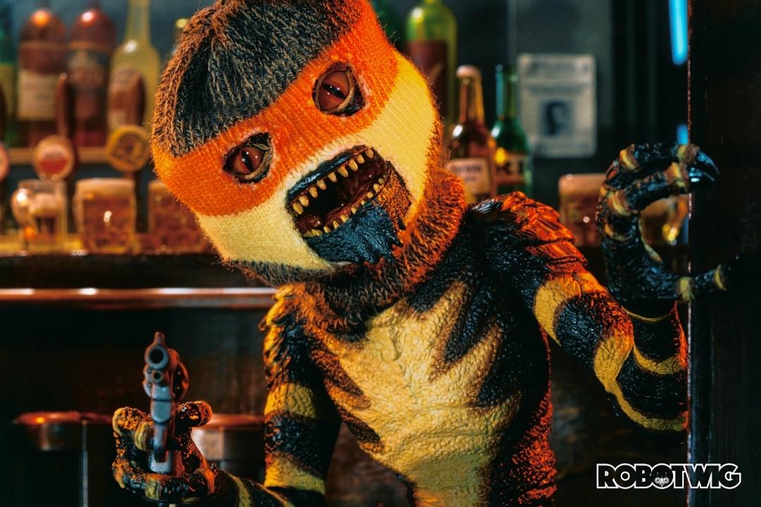 Gremlin in a bar wearing a balaclava holds a gun up at you
