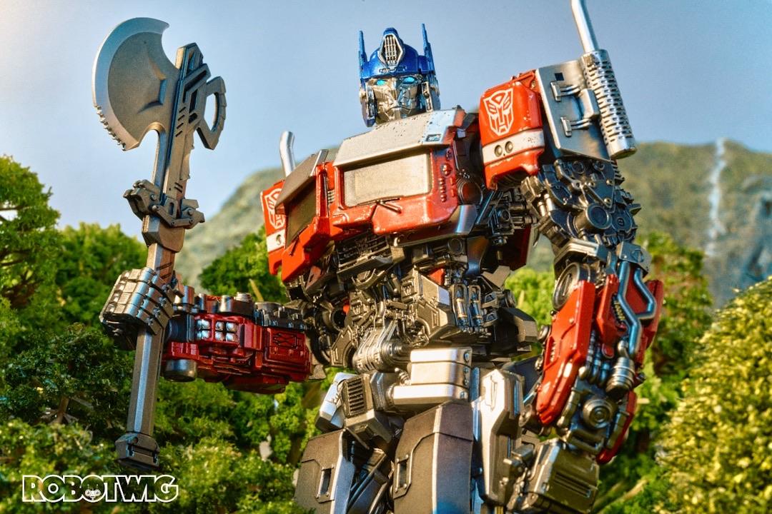 Optimus prime stands in a forest area armed with an axe