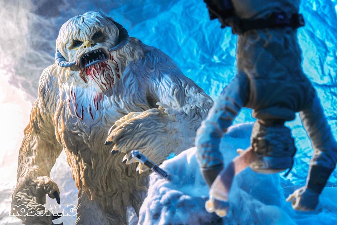 Luke hangs from the ceiling of the Wampa's ice cave his lightsaber stuck in the snow. The Wampa with blood around its mouth approaches him