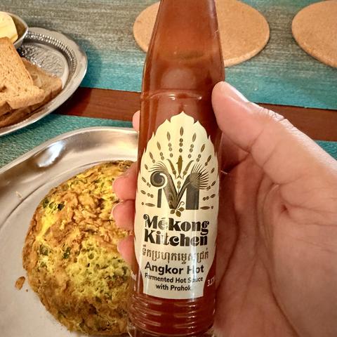 A photo of masala omelette with a lot of cut green chilies and an side of Mekong kitchen Angkor hot sauce from Cambodia