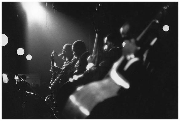 Eric Dolphy (with a bass clarinet), John Coltrane (soprano saxophone), Jimmy Garrison and Reggie Workman (contrabass). The photography, entitled “Two Bass Kit”, is by Herb Snitzer, taken during rehearsals at Village Vanguard, November 1961.