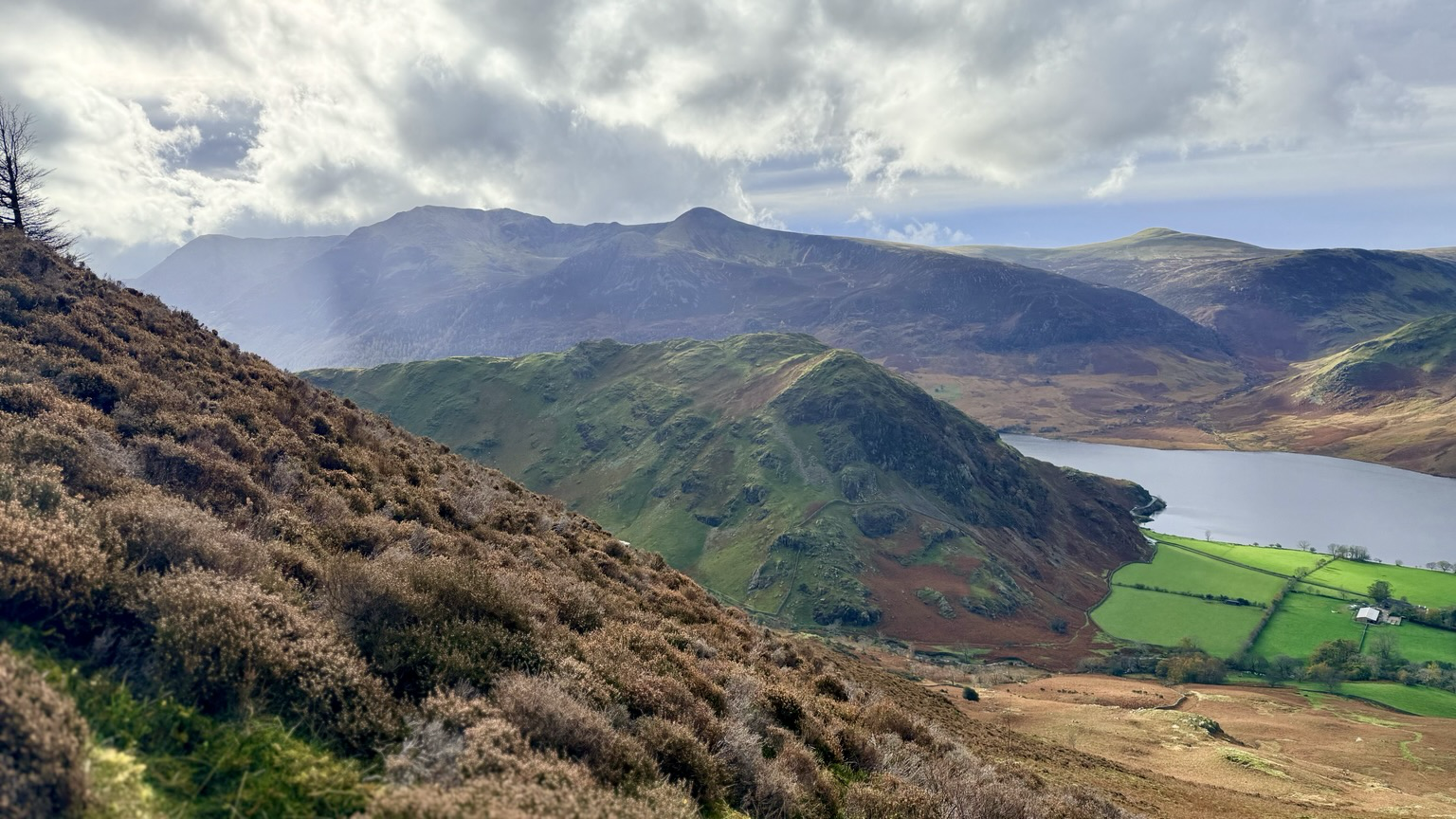 Layered mountains with a dramatic sky. Colours are Autumnal, there is a lake in centre right between the hills.