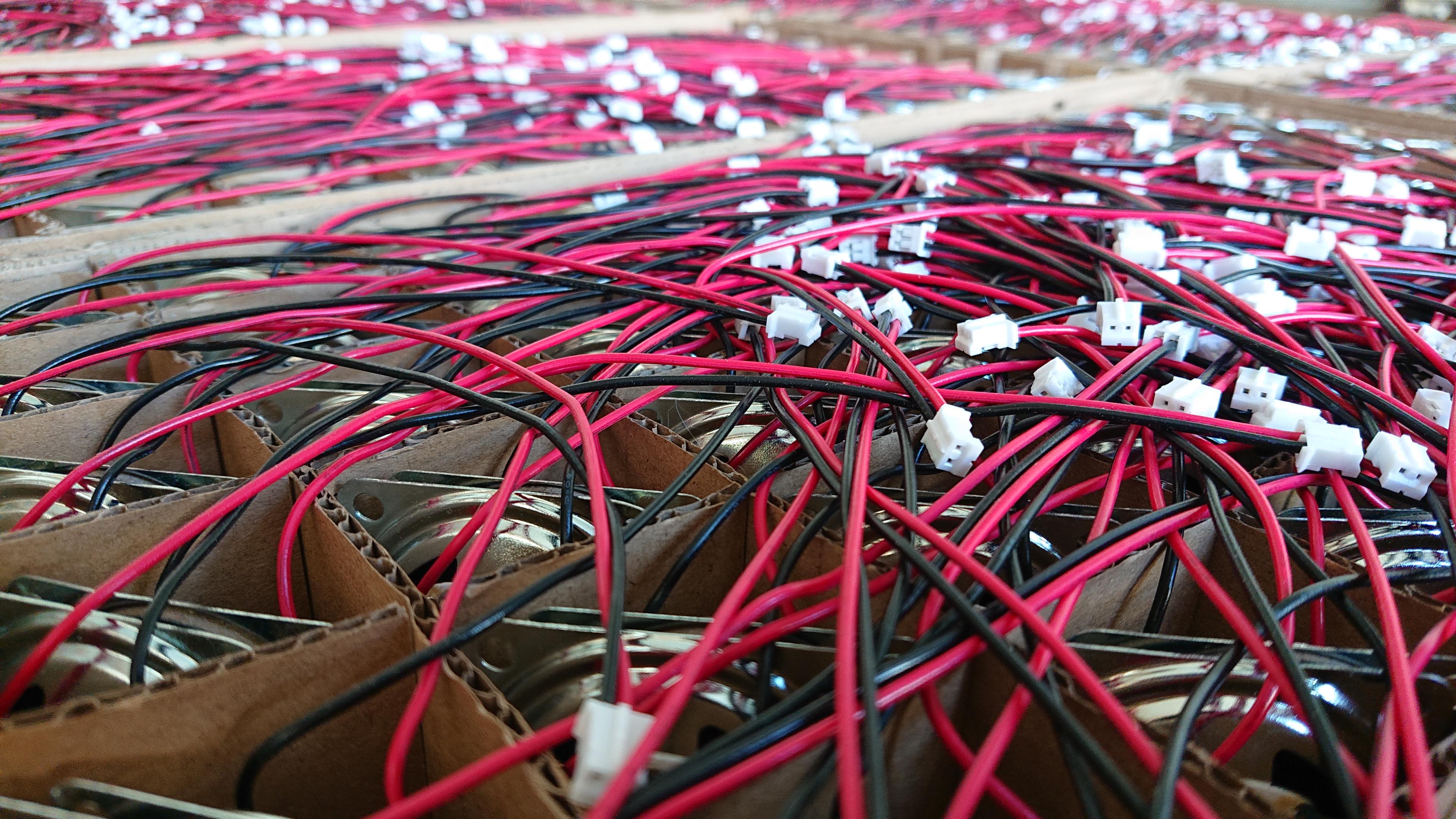 Looking out across a sea of speakers, all slotted in pairs into a grid of gaps in the cardboard packaging.
Not that it's too easy to spot that they're speakers, the silver of the frame is just about visible in the ones nearest to us, and mostly it looks like a massed tangle of red and black wires dotted with white JST connectors