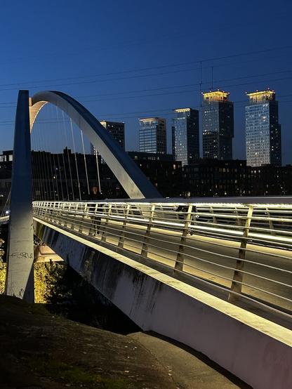 Valaistu kävelysilta, iltanäkymä kaupunkiin ja tornitaloja