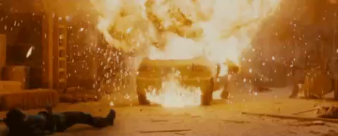 A fiery explosion brings a whole car up and slams it over a defenseless person on the ground.