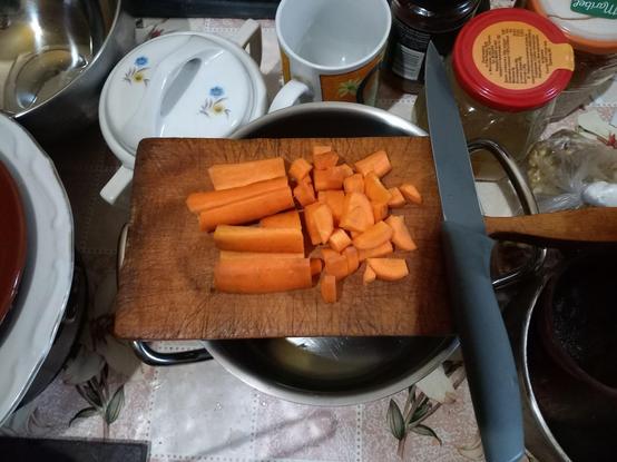 A carrot, sliced at length and half-chopped, on a wooden chopping board next to a knife.