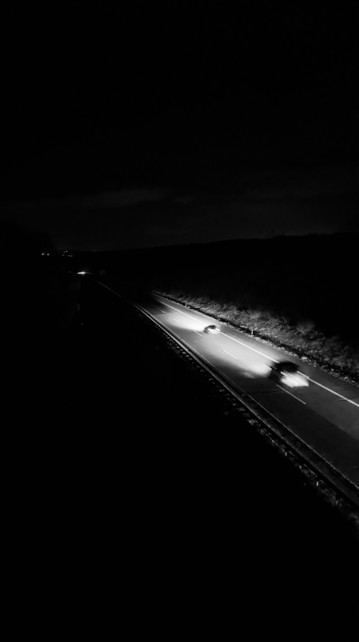 A nighttime black and white image of a highway with the headlights of moving cars illuminating the road.