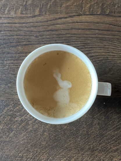 A cup of coffee with foam art resembling a silhouette, on a wooden table.