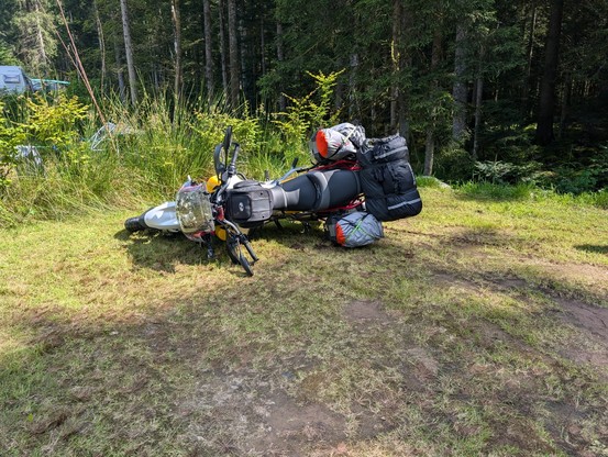 Vollgepacktes Motorrad, das auf einem Camping-Stellplatz mit Wiese auf der Seite liegt.