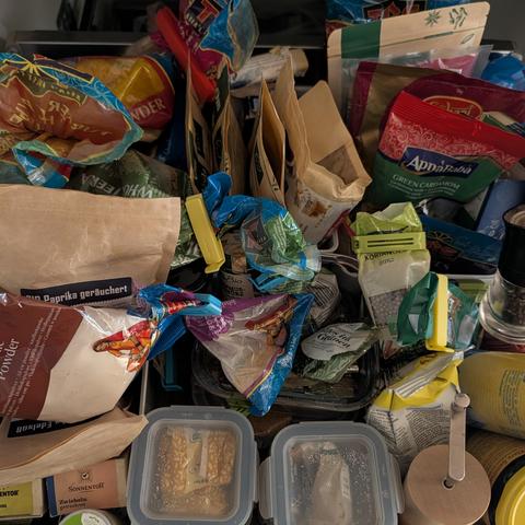 Blick in eine vollgepackte Küchenschublade mit Gewürztüten, Gläsern und kleinen Frischhaltedosen. Viele geöffnete Beutel sind mit bunten Verschlussclips fixiert. Sichtbar sind unter anderem geräucherter Paprika, grüner Kardamom, Koriander und Zwiebeln.