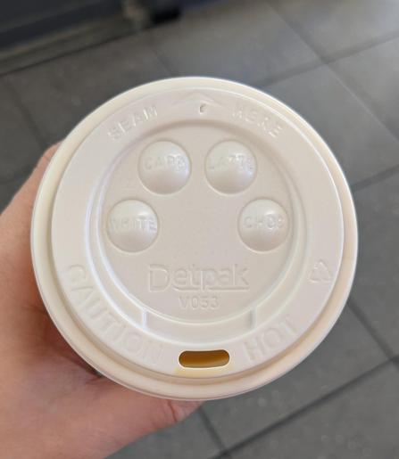 the lid of the coffee cup has four divets in a half-circle that look like eyes together with the mouth hole that looks like a slightly smilng mouth