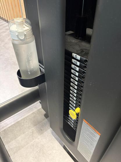 Blick auf die Gewichsscheiben eines Fitnessgerätes. Es sind 110 kg eingestellt. In einer Halterung am Gerät sieht man eine Wasserflasche