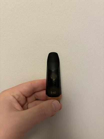 Clarinet mouthpiece with a worn-out Vandoren logo and faded color in places not covered by a ligature or a patch.