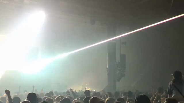 Underworld live in a big warehouse in Manchester with big lasers piercing the smoke and air above the heads of the crowd
