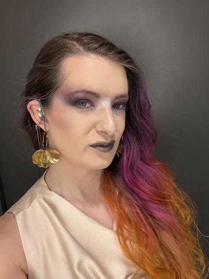 Hazel looks at the camera wearing a smokey eye and cream ombre dress, and gold earrings