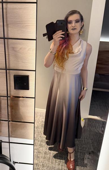 Hazel looks at the camera in a mirror selfie wearing a smokey eye and cream ombre dress, and gold earrings