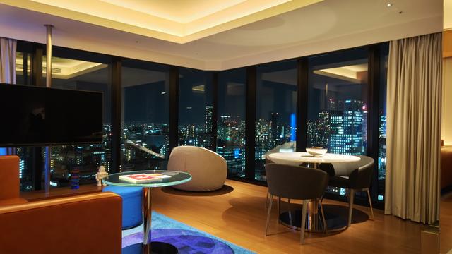 A photo at night of a lit hotel suite sitting area with a corner panoramic view of the city of Osaka