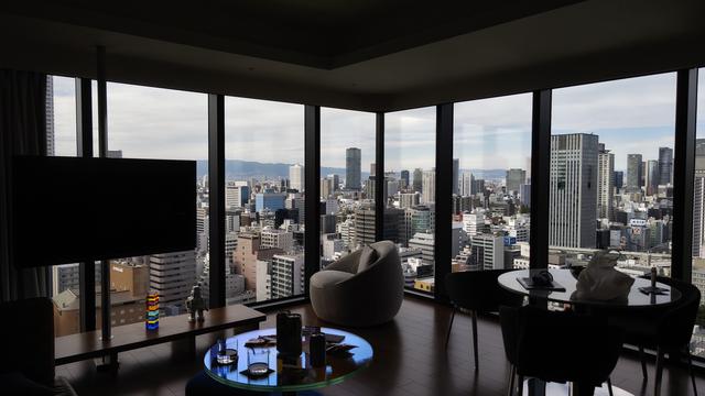 A photo during the day of an unlit hotel suite sitting area with a corner panoramic view of the city of Osaka