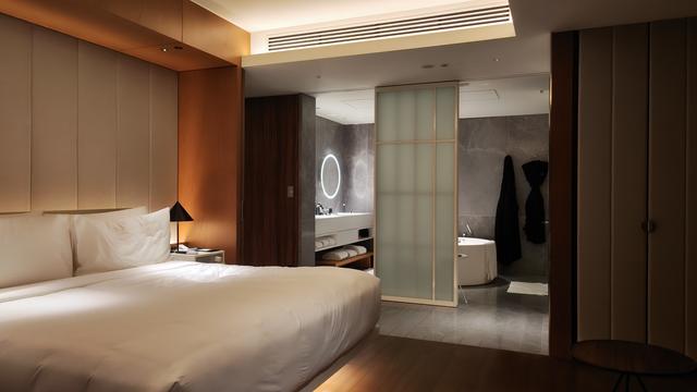 a photo at night of a white bed and bathroom with nice lighting in a hotel room
