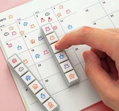 Button stamps that show little icons to represent the weather. They are being used to stamp a calendar.