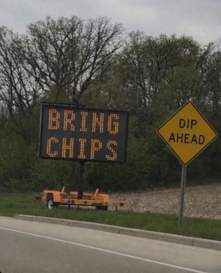 A road sign reads ‘dip ahead’ and nearby stands a construction sign reading ‘bring chips’.