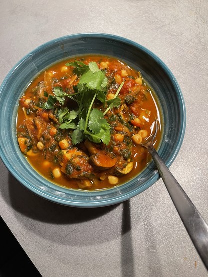 A bowl of curry with mushrooms, spinach, chick peas and cilantro 