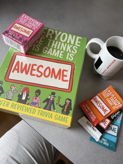 Game package for a board or card game called „everyone else thinks this game is awesome“. Also some expansion card packs for the game and a cup of coffee 