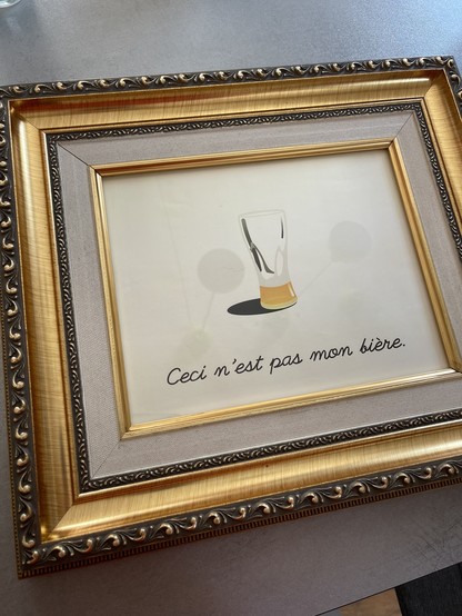 A gold frame containing an image of a mostly empty glass of beer. Below: Ceci n‘est pas mon bière. 