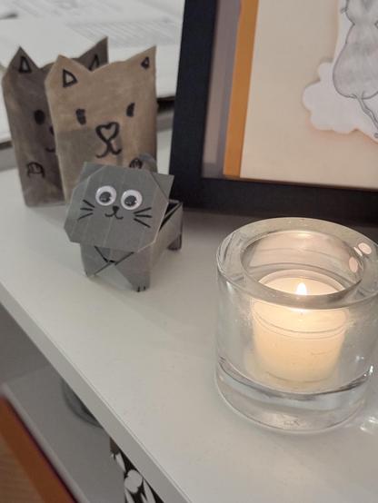 A candle in front of tiny little cat figurines made by friends‘ kids 
