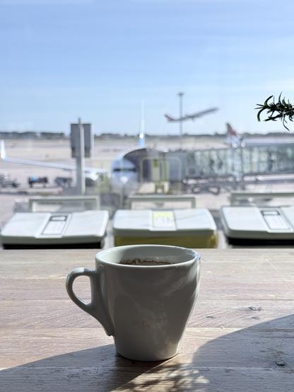 Foreground: a cup of espresso. Background: an airplane at the airport shoulder. Far background: another airplane that list departed, hanging in the air 
