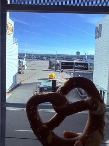 A pretzel being held in front of another airport (MUC)