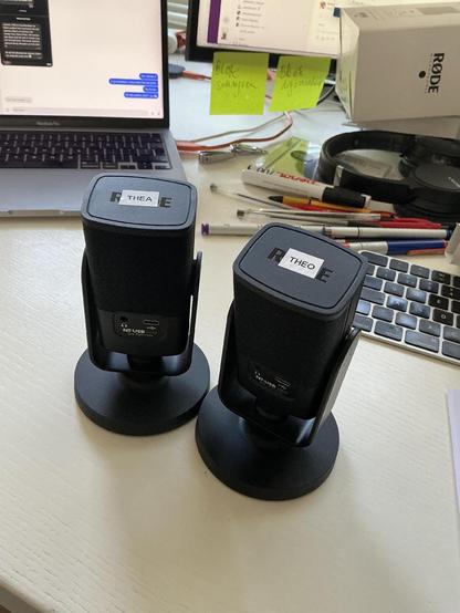 Twee identieke microfoons met elk een naamsticker. De een heet Theo, de ander heet Thea.
