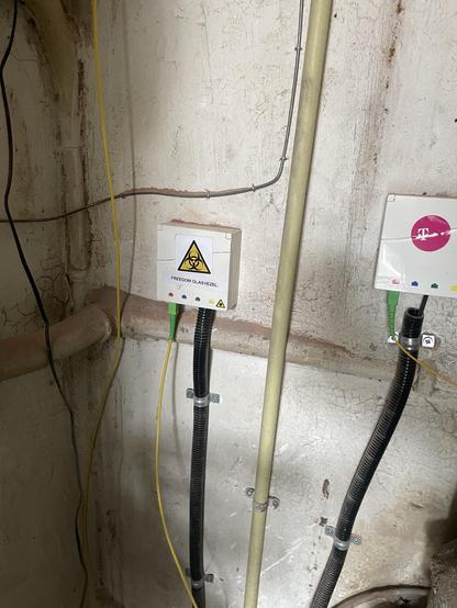 Paulze meterkast met twee glasvezeldoosjes: een voor Paul en een voor de buurman. Op het kastje van de buurman zit nog een T-Mobile-sticker. Op Paulze kastje zit een sticker met een biohazardlogo en tekst "Freedom Glasvezel".