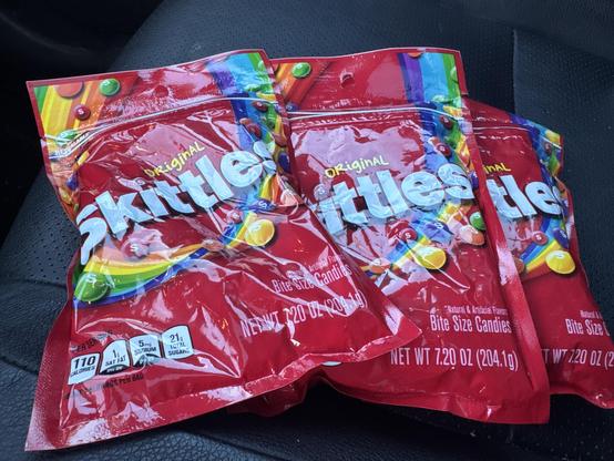 Photo of three bags of skittles on a car seat. 