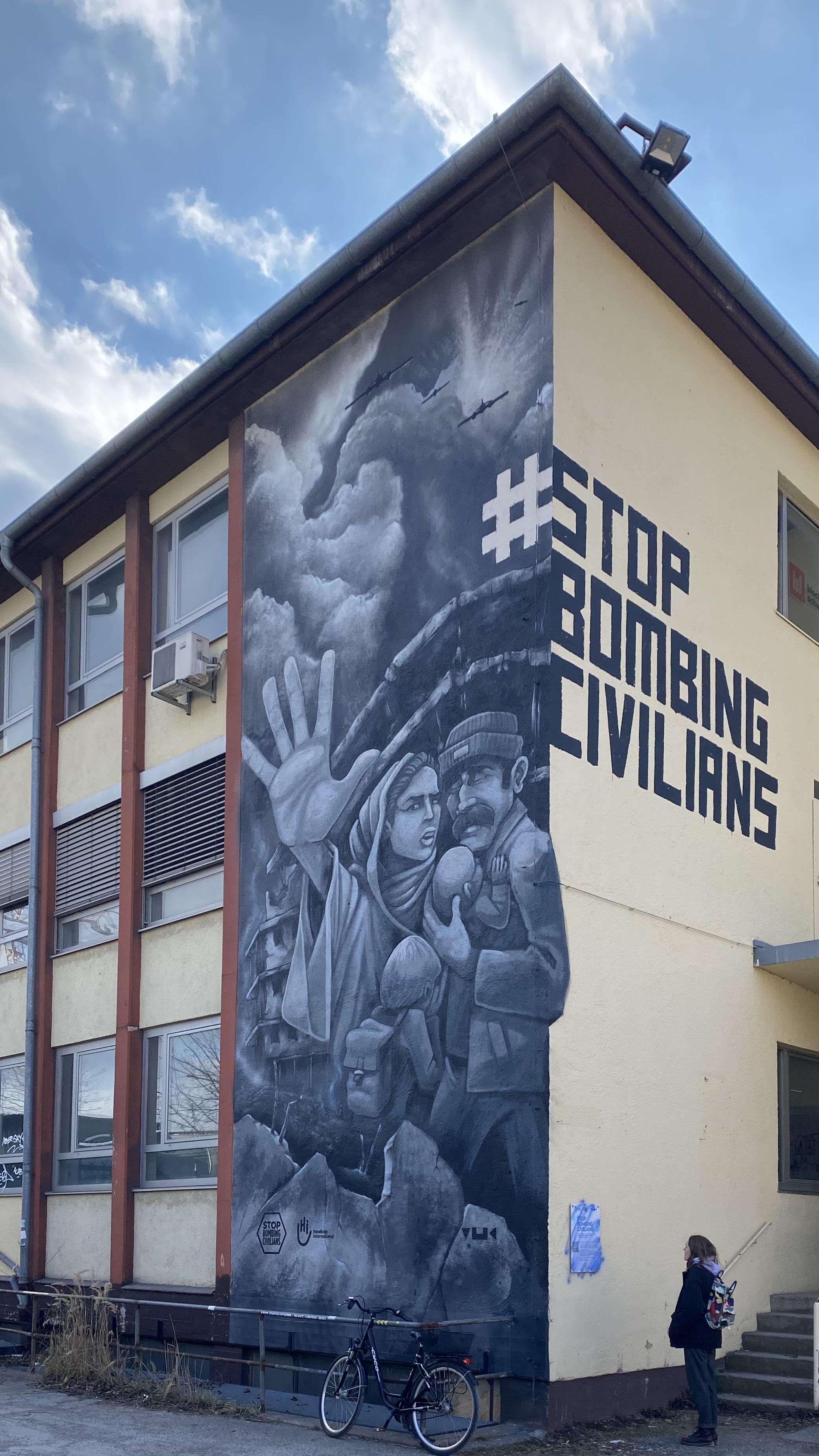 Picture of STOP BOMBING CIVILIANS mural I took in 2022. It depicts a family in front of a destroyed building with the woman raising her hand to say STOP.