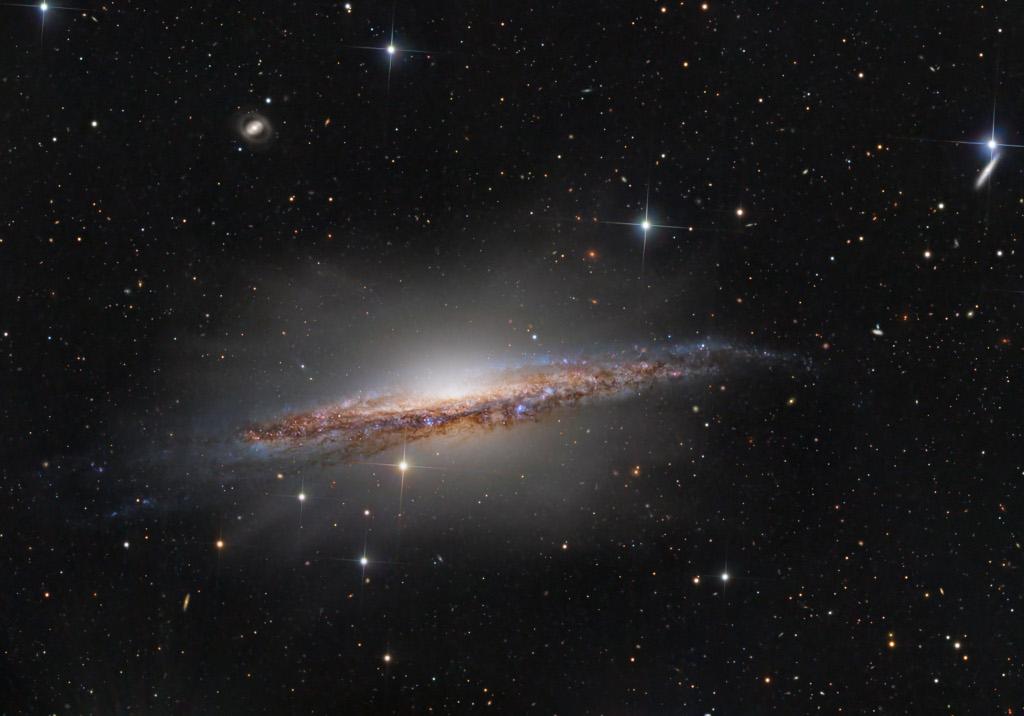 NASA Astronomy Picture of the Day, November 27, 2025
https://apod.nasa.gov/apod/ap251127.html

NASA-provided image caption:

Portrait of NGC 1055
Image Credit & Copyright: John Hayes

Explanation: Big, beautiful spiral galaxy NGC 1055 is a dominant member of a small galaxy group a mere 60 million light-years away toward the aquatically intimidating constellation Cetus. Seen edge-on, the island universe spans over 100,000 light-years, a little larger than our own Milky Way galaxy. The colorful, spiky stars decorating this cosmic portrait of NGC 1055 are in the foreground, well within the Milky Way. But telltale pinkish star forming regions and young blue star clusters are scattered through winding dust lanes along the distant galaxy's thin disk. With a smattering of even more distant background galaxies, the deep image also reveals a boxy halo that extends far above and below the central bulge and disk of NGC 1055. The halo itself is laced with faint, narrow structures, and could represent the mixed and spread out debris from a satellite galaxy disrupted by the larger spiral some 10 billion years ago.