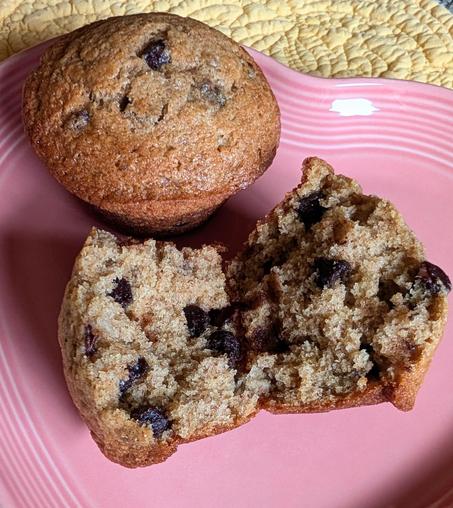 Two banana chocolate chip muffins. One is broken in two. They are on a pink heart shaped plate.