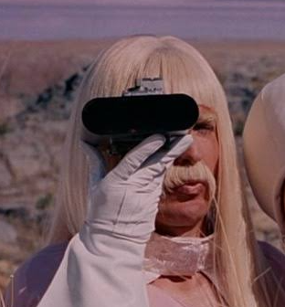 Blonde man with long moustache looking through black binoculars with white gloves, in a desert setting.
Gentlemen Broncos, 2009