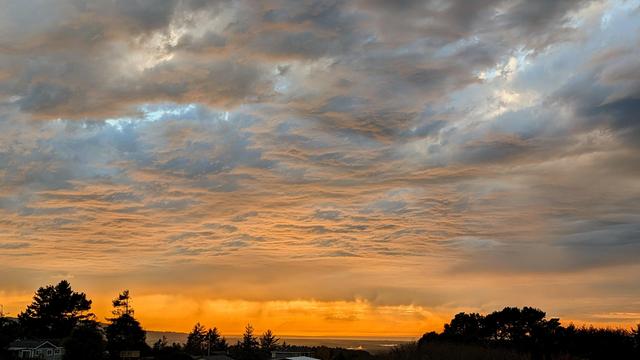 A late afternoon sky that is heavy with clouds. It looks like there might be rain falling over the Pacific Ocean. The sun is turning the sky yellow.