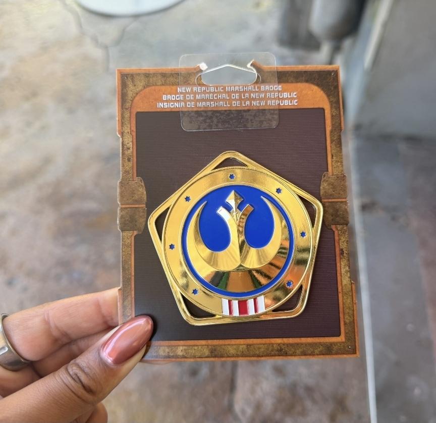 Five sided gold badge featuring the star wars resistance symbol. 7 stars around the edge and red and white stripes at the bottom. Its big. Looks like maybe 3 inches.