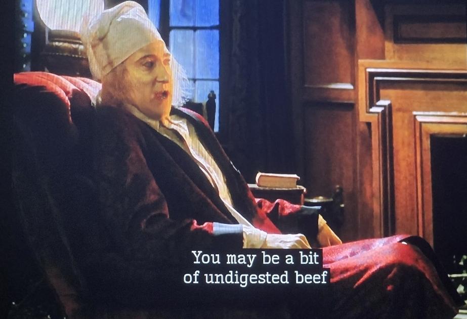 Data as Ebenezer Scrooge sitting in a velvet armchair by a fireplace. He speaks to a ghost and says: You may be a bit of undigested beef.