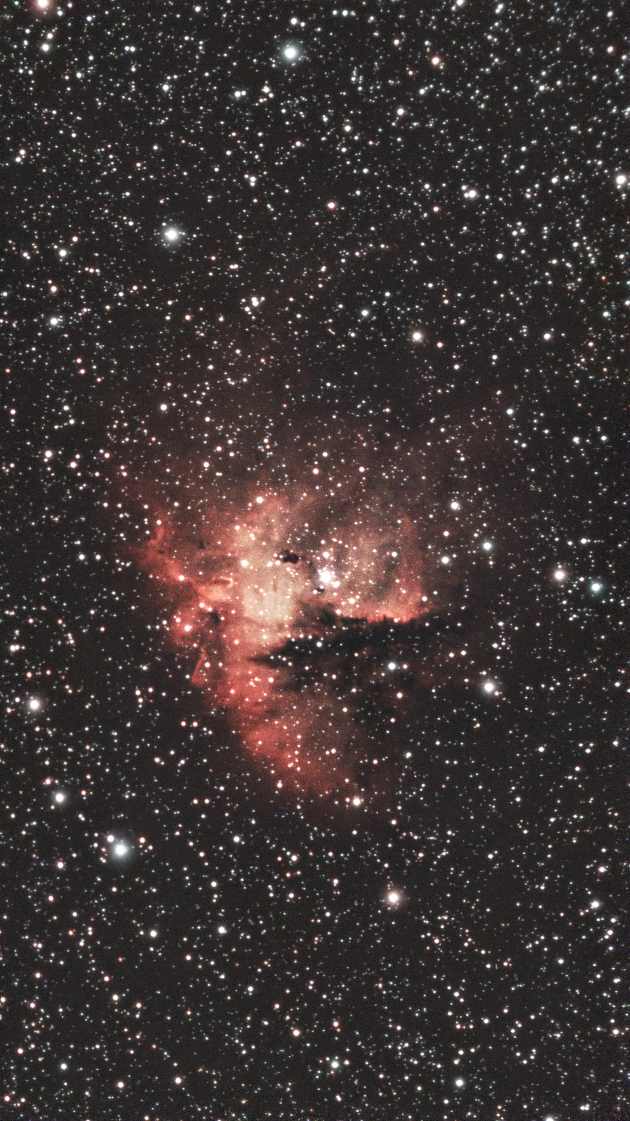 NGC 281, a red nebula in Cassiopeia. It has the vague "pie missing a slice" shape of pacman with either a bright star or  a dark dust cloud serving for the eye. Lots of interesting dust clouds cause sharp linear features to appear.