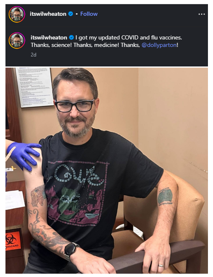Instagram post by verified account @itswilwheaton showing actor Wil Wheaton receiving a vaccination while seated in a medical clinic.
•	Wheaton wears black-framed glasses, a black graphic T-shirt and a smartwatch.
•      Wil's tee shirt says The Cure and has a stylized picture of Robert Smith on it
•	His tattooed arms are visible, with his left sleeve rolled up to expose his upper arm.
•	A healthcare worker wearing a purple medical glove holds his upper arm during the vaccination.
•	Wheaton sits in a beige chair, smiling slightly towards the camera.
•	The clinic has beige walls, medical paperwork and a sharps disposal container.
•	Caption reads: “I got my updated COVID and flu vaccines. Thanks, science! Thanks, medicine! Thanks, @dollyparton!”
•	Post was shared two days earlier.