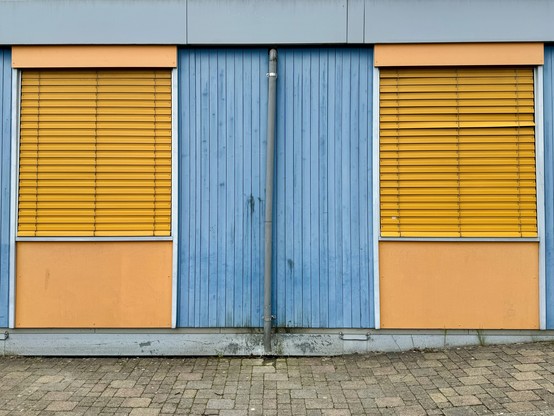 A blue double door flanked by two windows with yellow blinds, set in a building with blue and beige walls.