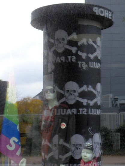 Litfasssäule mit Aufdruck des Totenkopfs St. Pauli spiegelt sich in einem Fenster