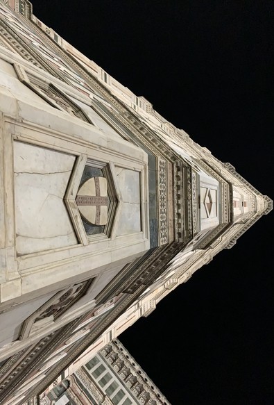 Ornate architectural detail from a tall building, captured at night against a dark sky. Giotto's Campanile is a free-standing campanile (bell tower) that is part of the complex of buildings that make up Florence Cathedral on the Piazza del Duomo in Florence, Italy.