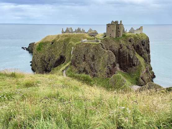 Ruins of an ancient castle perched on a grassy cliff overlooking the sea.